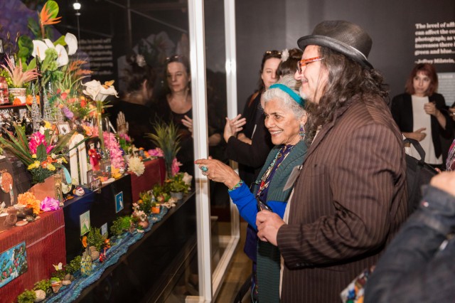 Older woman and man in hat looking intently at a colorful altar in Becoming Los Angeles exhibition