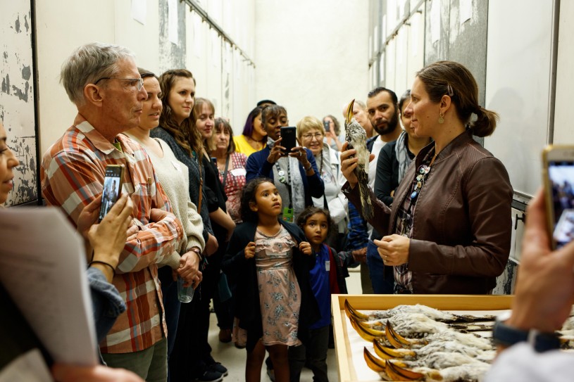 A large group of people look at a bird specimen that is held by an NHM scientist