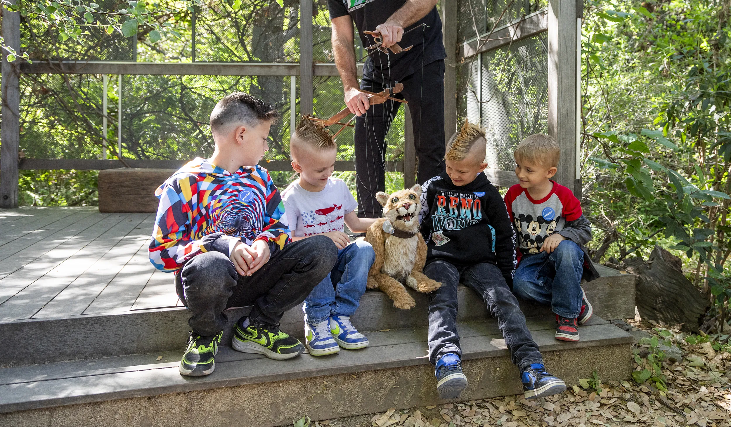 Children sitting on either side of a puppeteer holding the strings of miniature mountain lion puppet