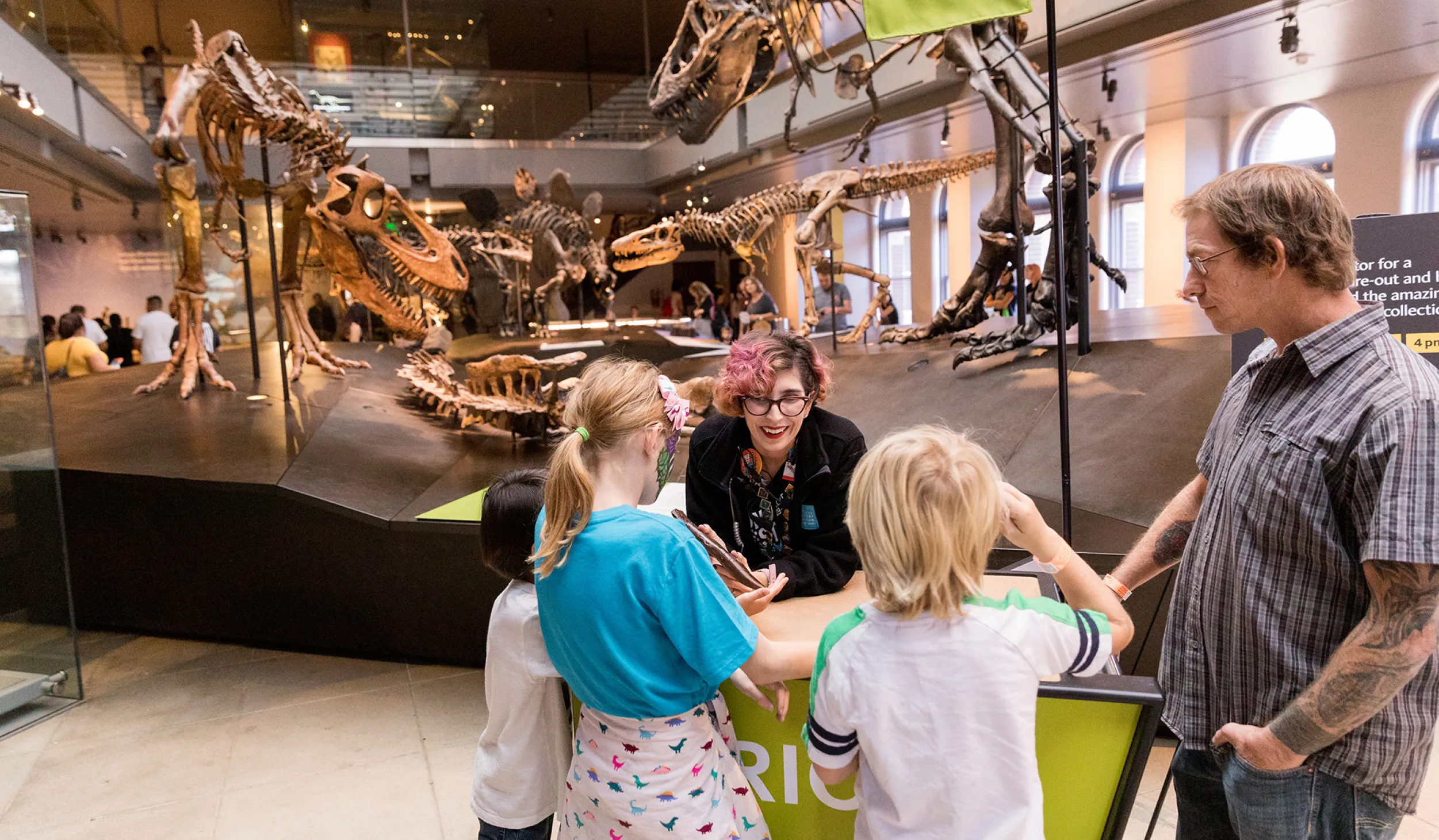 Museum Educator showing a specimen to visitors gathered around a cart