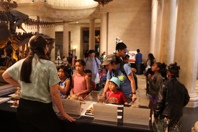 Exhibit table in the museum foyer with kids gathered around fossils.