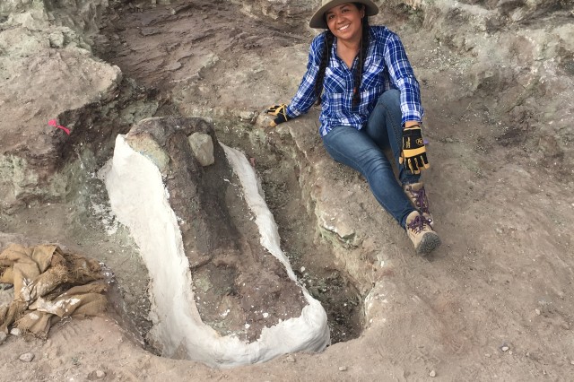 Valeria Jaramillo sitting next to a fossil specimen at an excavation site. 