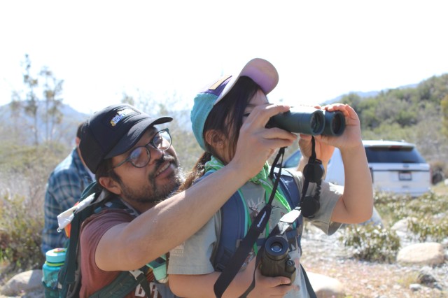 Closeup of a father holding binoculars up to his  daughter as she looks through the lens