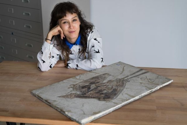 Jingmai O’Connor with her head in her hand and other arm on a table with a fossil in front of her