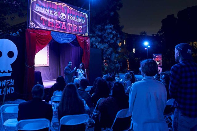 Visitors watching a performer in front of a stage with red curtains