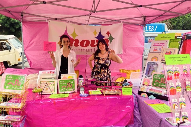 Two people making peace signs, standing behind a pink table in a pink tent