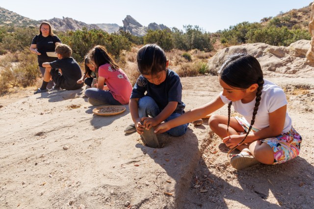 Children in a line grinding acorns on a bedrock mortar at Vasquez Rocks