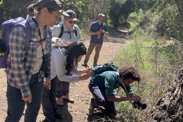 Allison Shultz with UNLAB participants crouching down to photograph specimens in grass