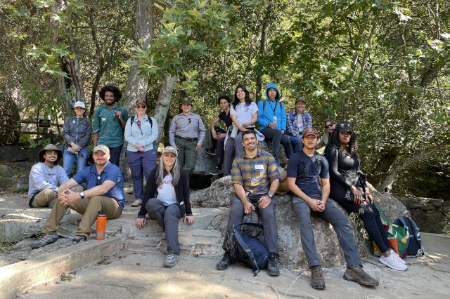 Group of students, NHM employees, and nature guide sitting and standing with trees in the background