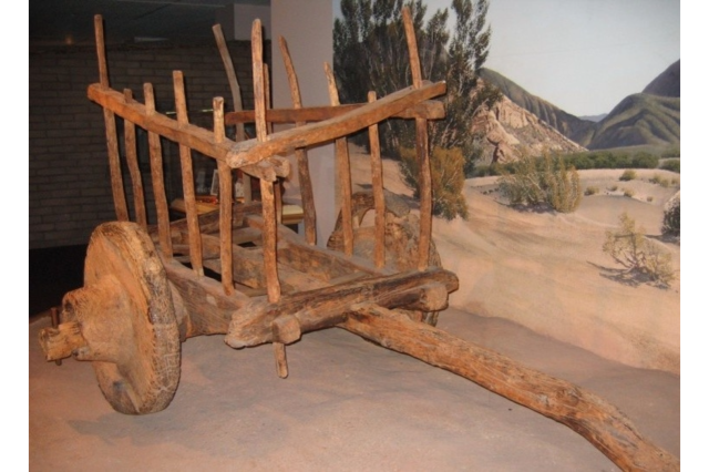 Wooden wagon with solid wheels, long yoke and thin slats forming three sides of the wagon, open in the back