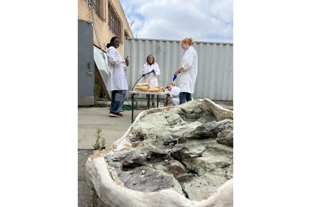 Interns outside at a table with dinosaur bones in a white jacket in the foreground