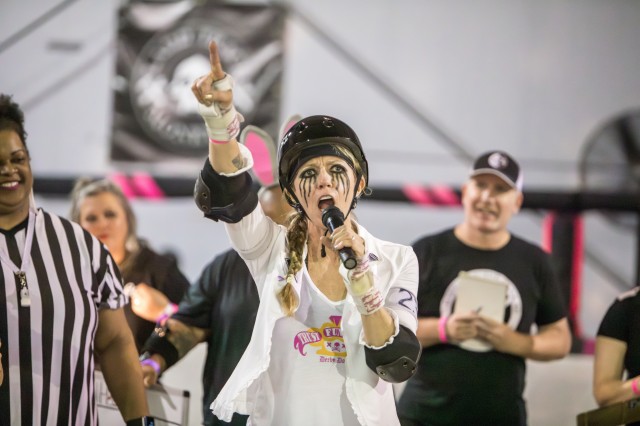 Evil E in roller derby uniform shouting into a microphone during a game