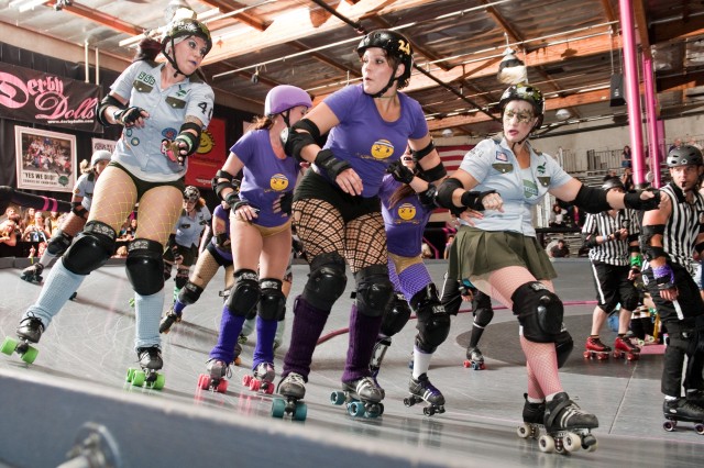 Roller derby players in purple vs. white push around each other on a banked track