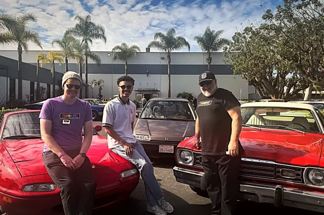 Randall, Rhoeby, and Mike sitting in front of their class cars