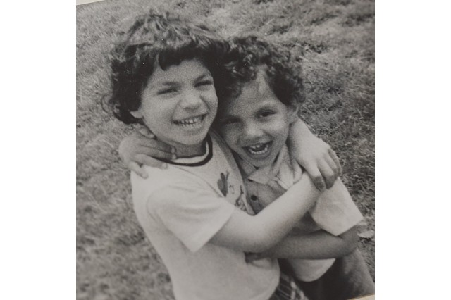 Black and white photo taken in the mid 1970s of two young brothers with dark, curly hair and white t-shirts, smiling and hugging each other.