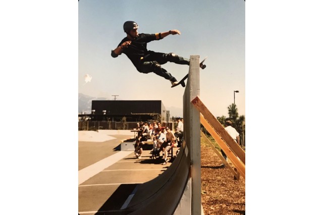 Skateboarder at the top of a wooden ramp in front of onlookers at a skate park