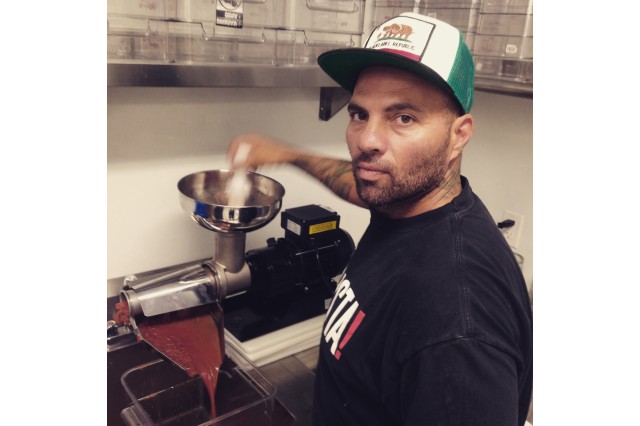 Man in a baseball cap and Pizzanista!-branded t-shirt weighs raw pizza dough on a kitchen scale.