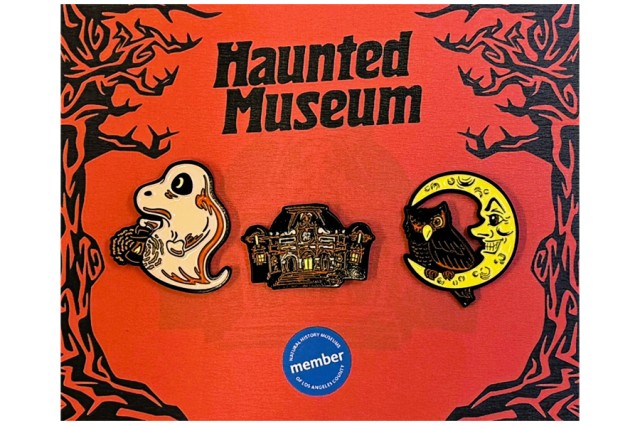 Ghost, mansion, and an owl in a crescent moon pins on a red background with black trees on either side and Haunted Museum in black letters above