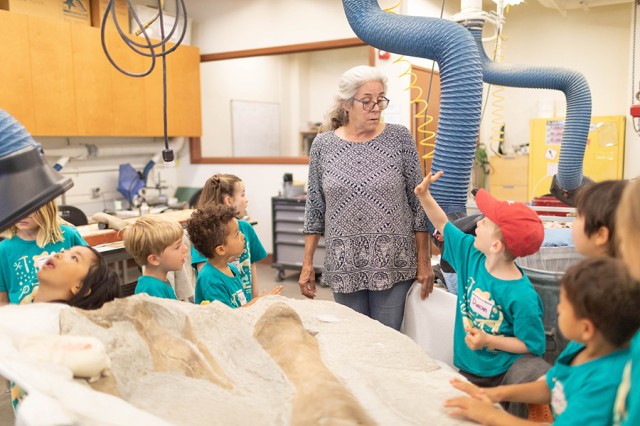 Maureen Walsh standing amongst children in green t-shirts around a table with dinosaur bones