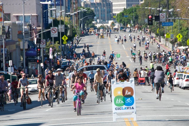 Dozens of cyclists on a six-lane city street, closed to cars, with the sign &quot;CicLAvia&quot; in front.