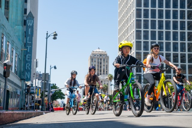 Four Asian-American children riding bikes along a downtown street with the Wiltern Theater marquee in the background.