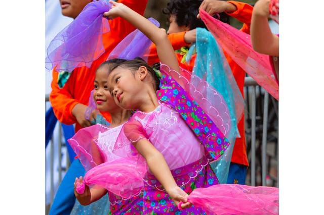 Two children in pink and purple dresses with one of their arms raised in the air