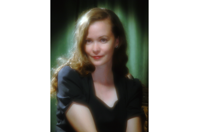 Head and shoulders portrait of Karie Bible with long wavy red hair and a black blouse