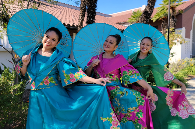Three women holding blue umbrellas and wearing blue, purple, and green dresses
