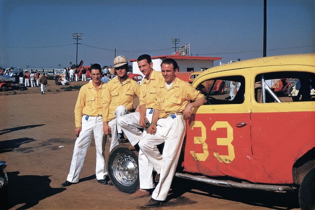 Four men in yellow shirts and white pants leaning against a yellow and red card with the number 33 on the door