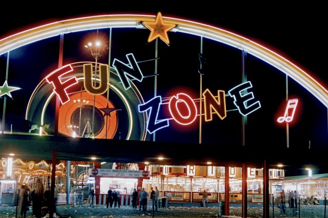 a rainbow arch over Fun Zone in neon, above an outdoor carousel and restaurant at night