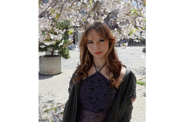 Chelsea Cook with long red hair, a black top, and pink cherry blossoms in the background