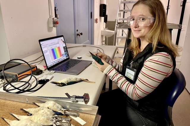 Jenna McCullough wearing clear goggles, sitting a table with a computer and bird specimens