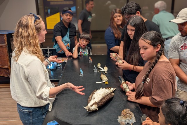 Jenna McCullough with hands face up, standing over a bird specimen on its back, and facing students