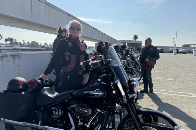 Row of bikers, dressed in black, standing by their motorcycles 