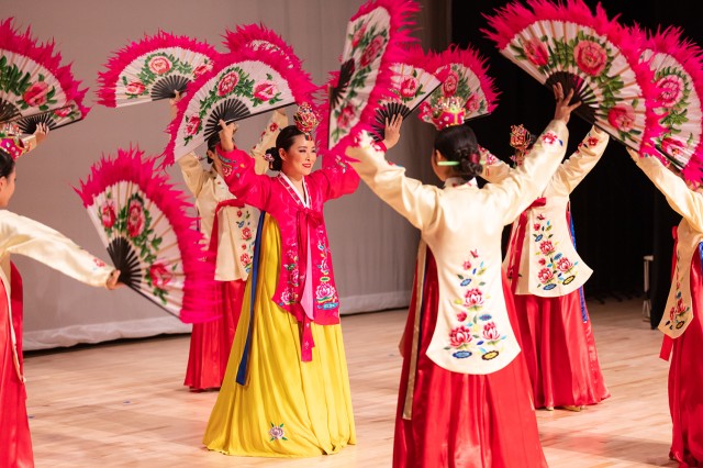 Dancers in fuchsia, red, and yellow and holding fans above their heads