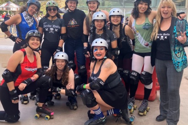 Eleven roller derby skaters posting together in their uniforms.