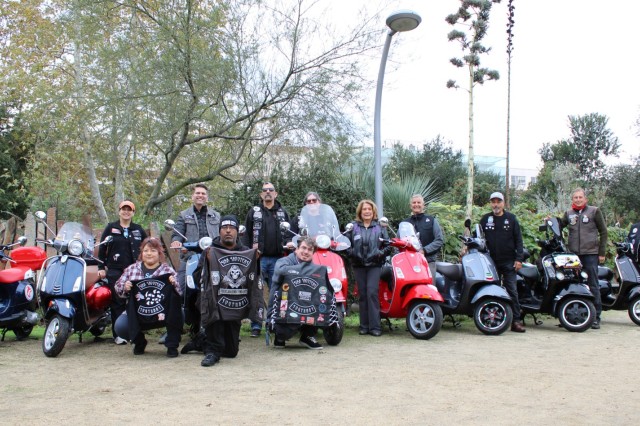 Vespa club members stand behind a row of their scooters.