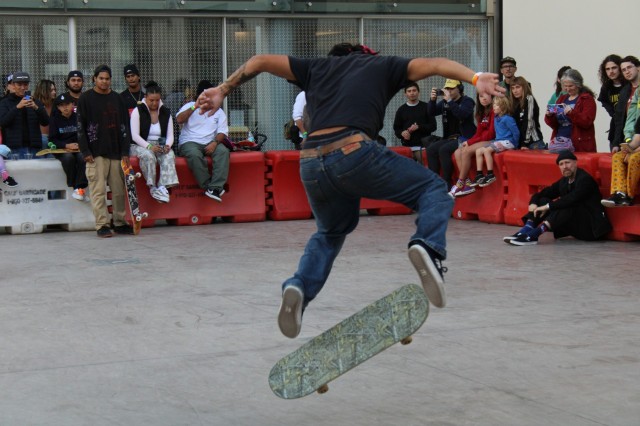 Skateboarder in black t-shirt and jeans flipping his skateboard with his feet in mid-air.