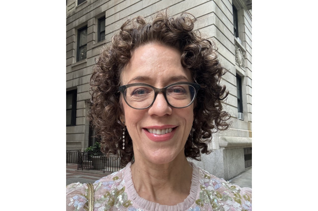 Head and shoulders portrait of Carin Greenberg facing the camera, wearing brown eyeglasses and a sequined shirt
