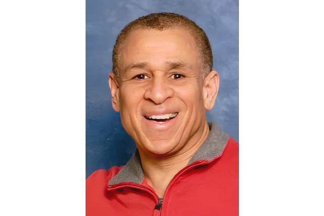 Head and shoulders of John Semper, smiling and wearing a red zip-up top