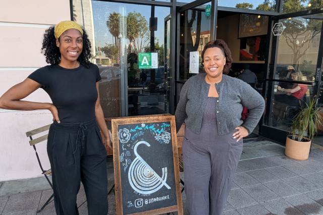 Amanda-Jane Thomas and Shanita Nicholas stand by an A-frame sign with the Sip & Sonder Logo outside their Inglewood location.