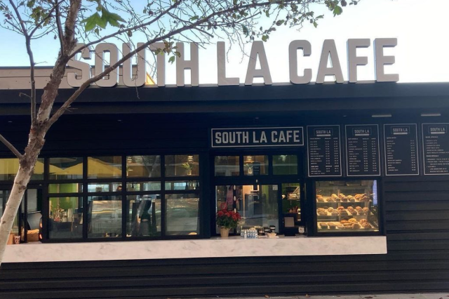 Store front of small coffee shop in a small gray building with "South LA Cafe" written in large block, white letters above the store.