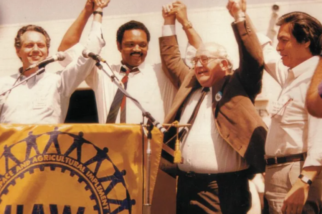 Four civil rights activities standing behind a UAW podium, raising clasped hands in the air.