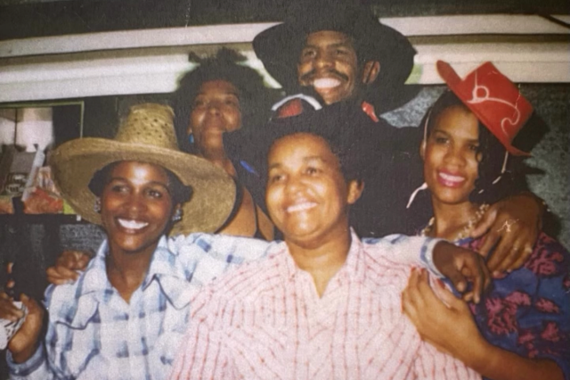 Five members of an African-American family, one man and three women, surrounding their mother, all smiling as they post together in Western-style outfits.