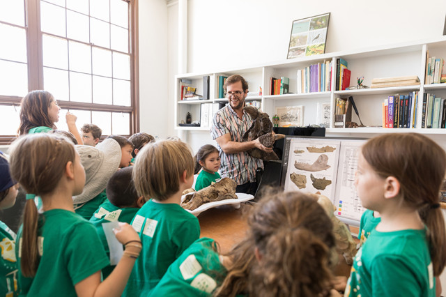 Children surrounding a collection manager holding up a fossil specimen