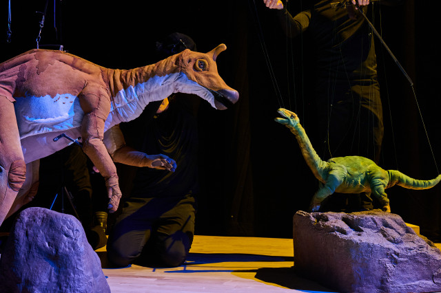 Horned dinorsaur puppet facing a smaller long-necked green dinosaur puppet
