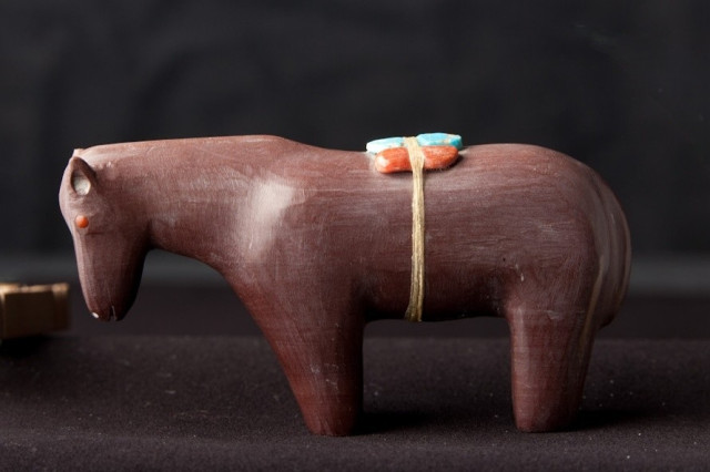 Small brown horse carved out of stone with a small red and green package wrapped around its back.