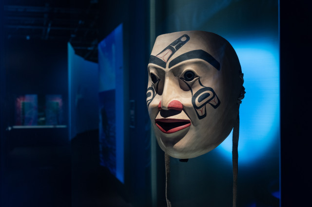 Large sculpture of a face with symbolic markings, in front of blue lighting