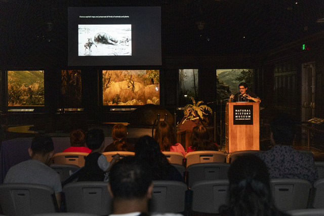 Crowd facing a speaker at a podium with a projection in the background
