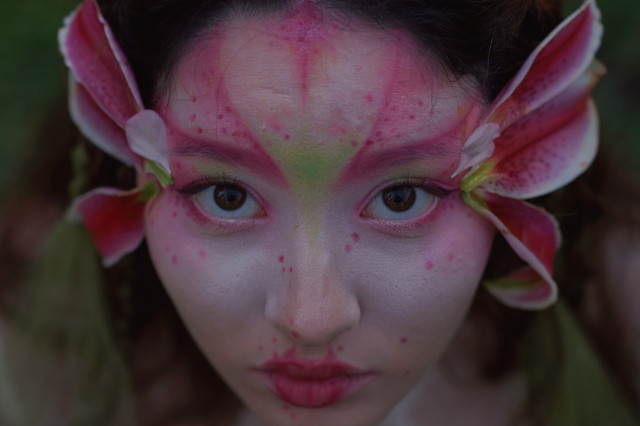 Close-up of woman's face with red makeup and flowers on the side of her head